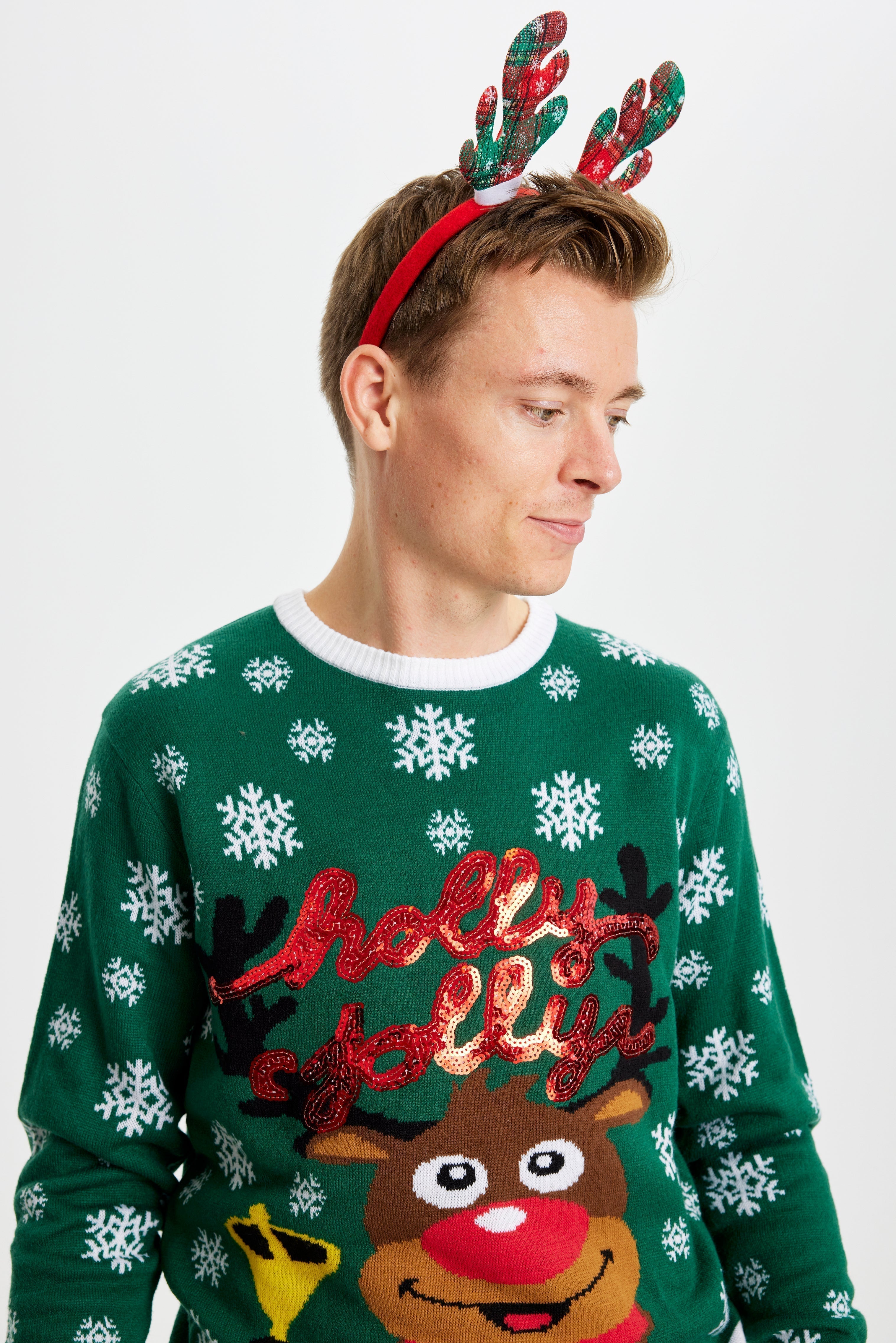 Un homme qui pose regarde de côté, vêtu d'un pull vert de Noël orné de Rudolph.